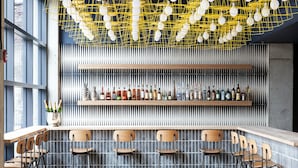 A bar area with wooden bar counters, metal chairs, and a variety of bottles on shelves. - The Boro Hotel (Long Island City)