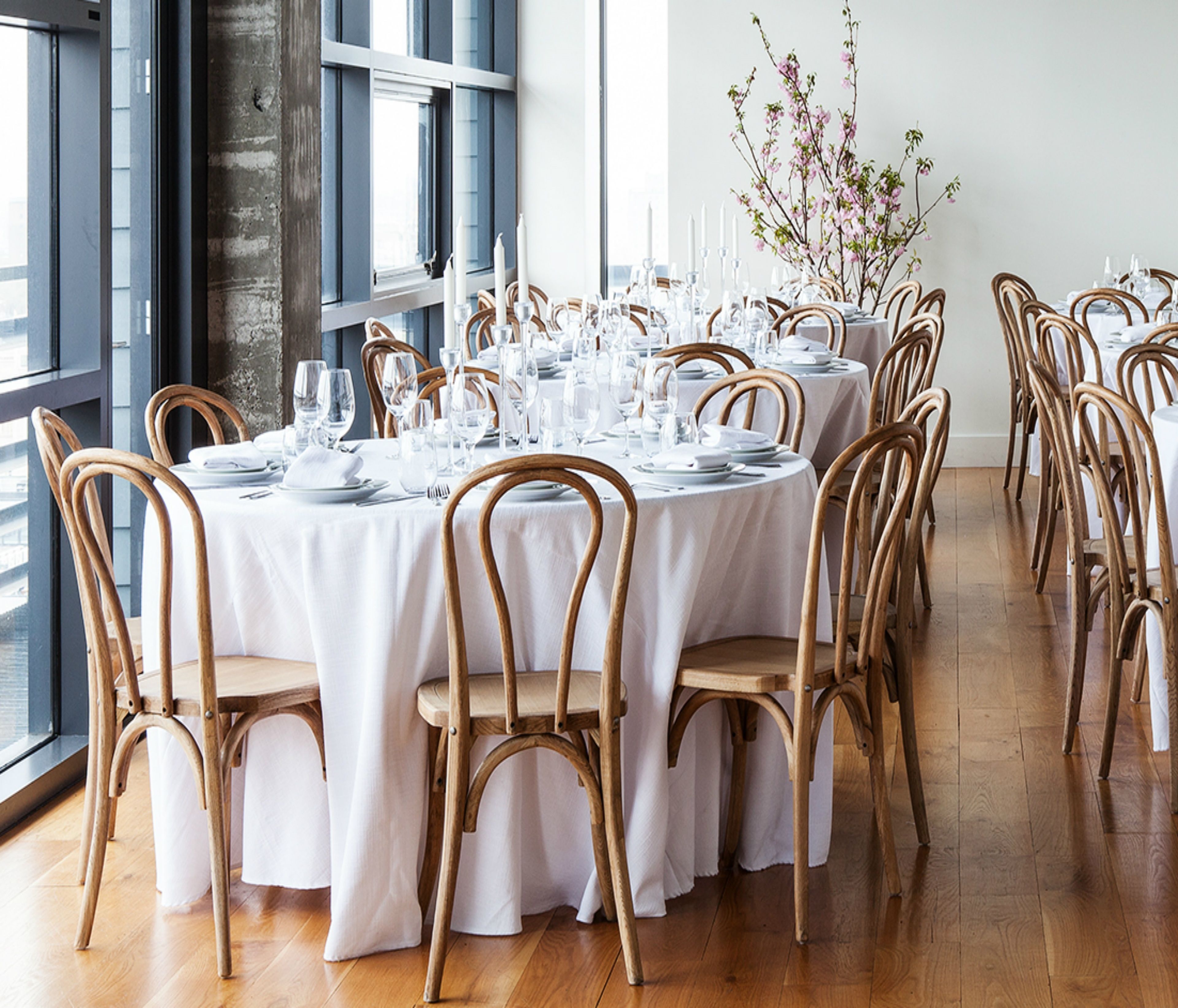 A dining area with round tables set for a meal, wooden chairs, and a large window providing natural light.