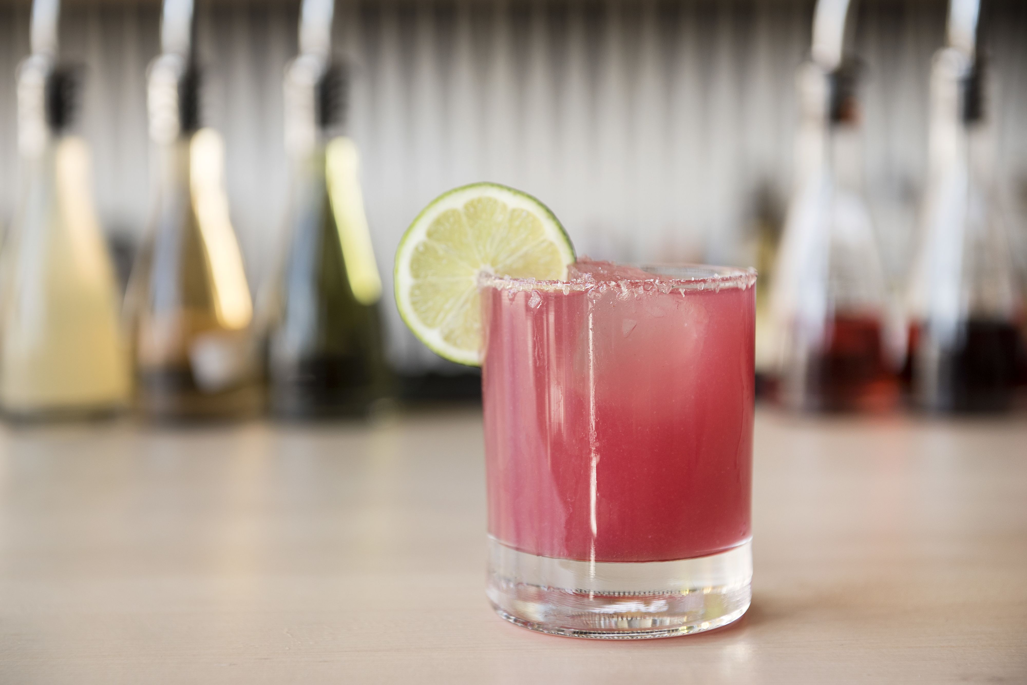 A glass of pink beverage with a lime slice on a bar counter.