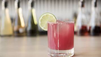 Ein Glas pinkfarbenes Getränk mit Limettenscheibe auf einer Bar.