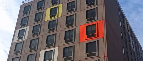 A multi-story building with a modern architectural design, featuring a prominent red and yellow facade, and a visible sign reading "BKLYN HOUSE".