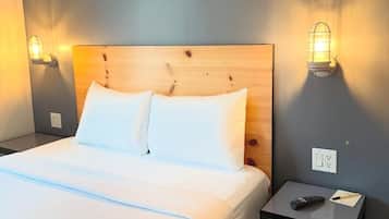 A hotel room with a bed, two bedside lamps, a nightstand with a remote control, and a wall socket.