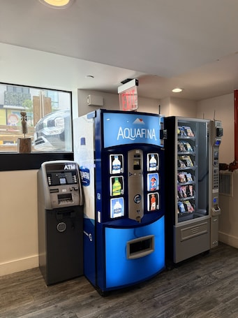 A blue Aquafina water dispenser and a vending machine in a room with a wooden floor.. Bklyn House