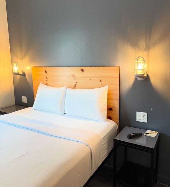 A neatly made bed with white linens, a wooden headboard, and two wall-mounted lamps.