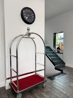 A hotel room with a metal cart, a wall clock, a staircase, and a view of the outside.