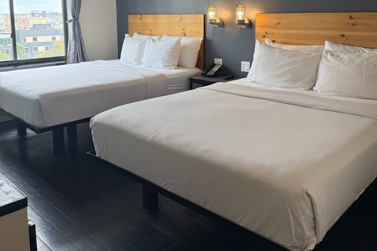 A hotel room with two beds, a large window, and a city view.