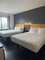 A hotel room with two beds, a large window, and a city view.