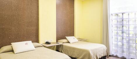 A hotel room with two beds, a small table, and a window with a view.