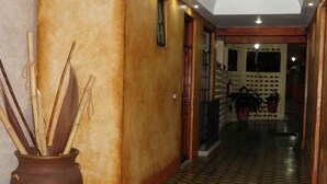 Um corredor com piso xadrez, um vaso grande com galhos e um teto com iluminação embutida.