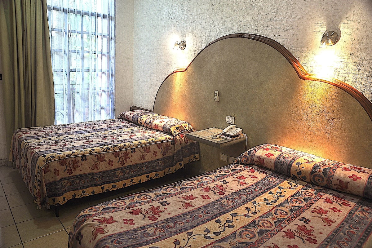 A room with two beds, a nightstand, a telephone, and a window with curtains.