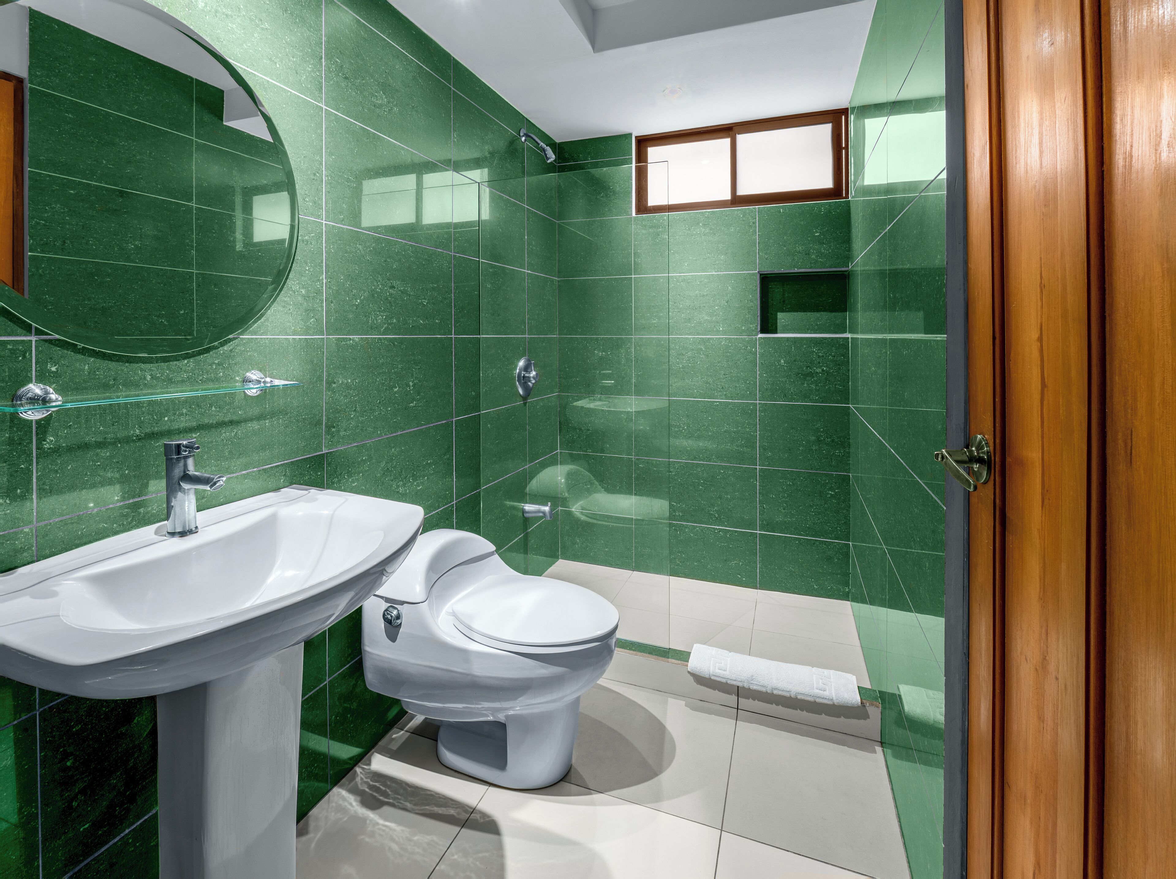 Casa de banho com azulejos verdes, uma pia branca, sanita e chuveiro.