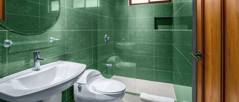 Casa de banho com azulejos verdes, uma pia branca, sanita e chuveiro.