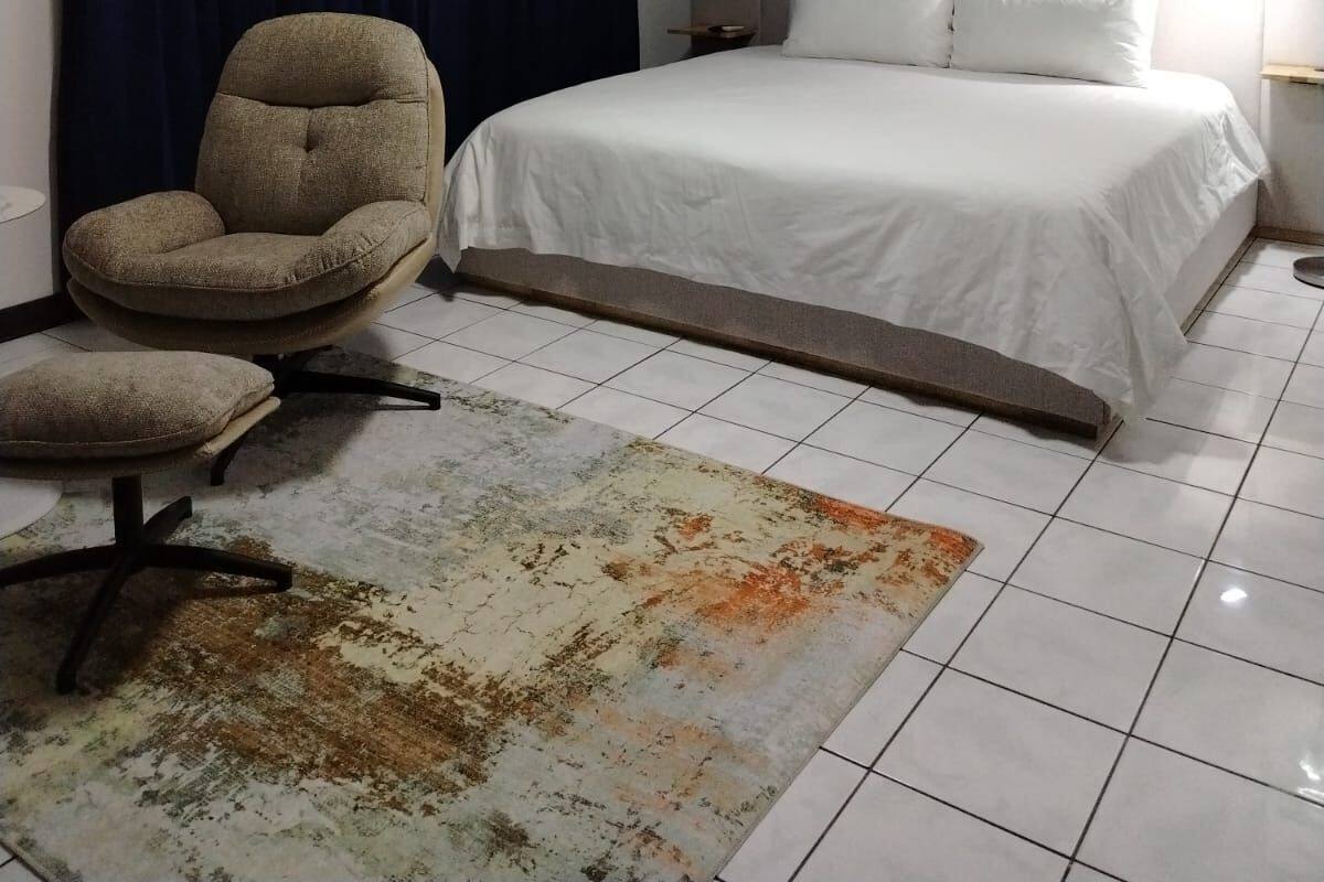 Quarto com cama, cadeira, tapete, relógio e cortina.