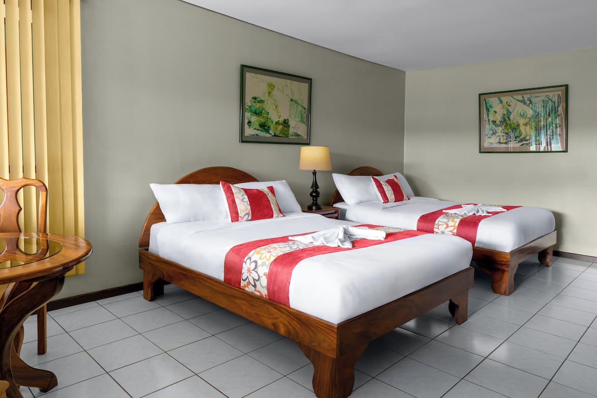 Quarto de hotel com duas camas de madeira, uma cadeira de madeira, uma mesa e duas pinturas nas paredes.