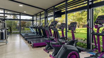 A gym with multiple treadmills and exercise bikes, large windows, and a view of greenery outside.