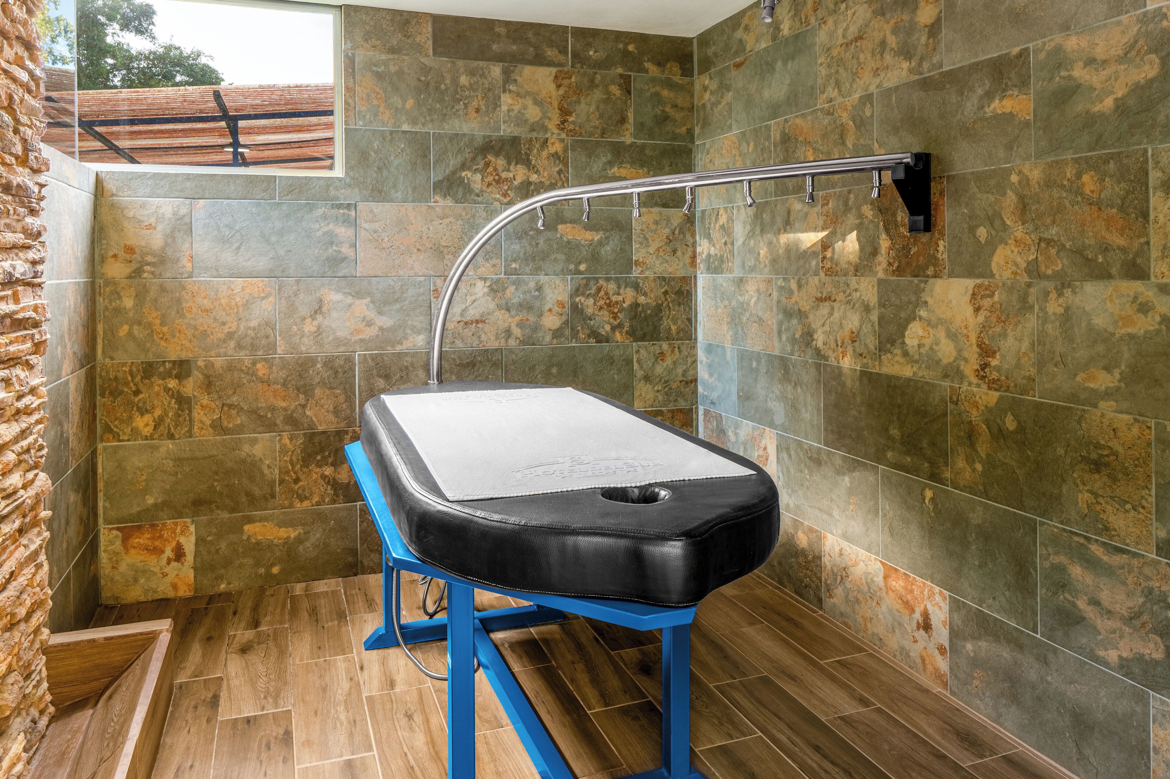 Una habitación con paredes de piedra, un banco de metal azul y una barandilla de metal.