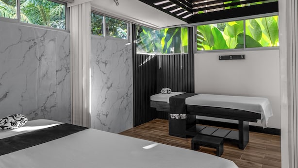 Un dormitorio moderno con una cama grande, una camilla de masaje y vistas a exuberante vegetación a través de amplios ventanales.
