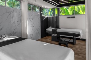 A modern bedroom with a large bed, a massage table, and a view of lush greenery through large windows. - Hotel del Sur (Daniel Flores)