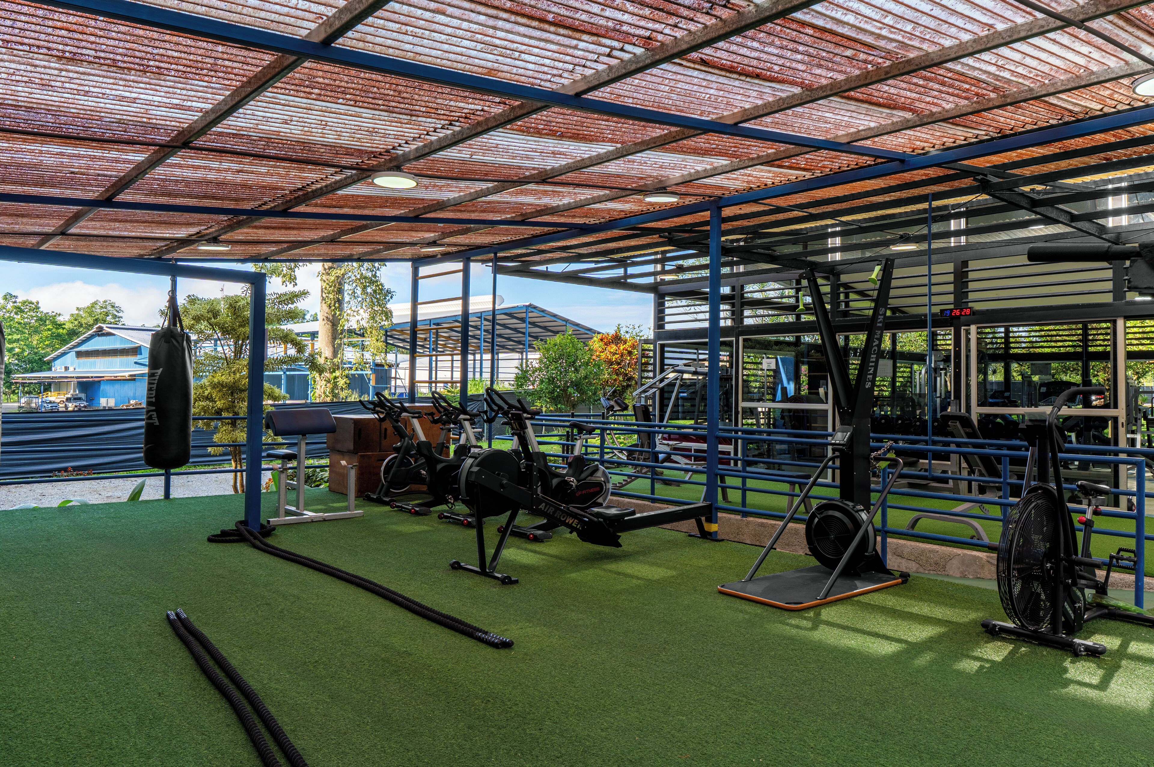 An outdoor gym with various exercise equipment, including a rowing machine, stationary bike, and weights.