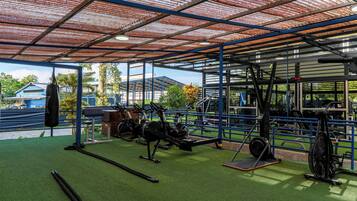 An outdoor gym with various exercise equipment, including a rowing machine, stationary bike, and weights.