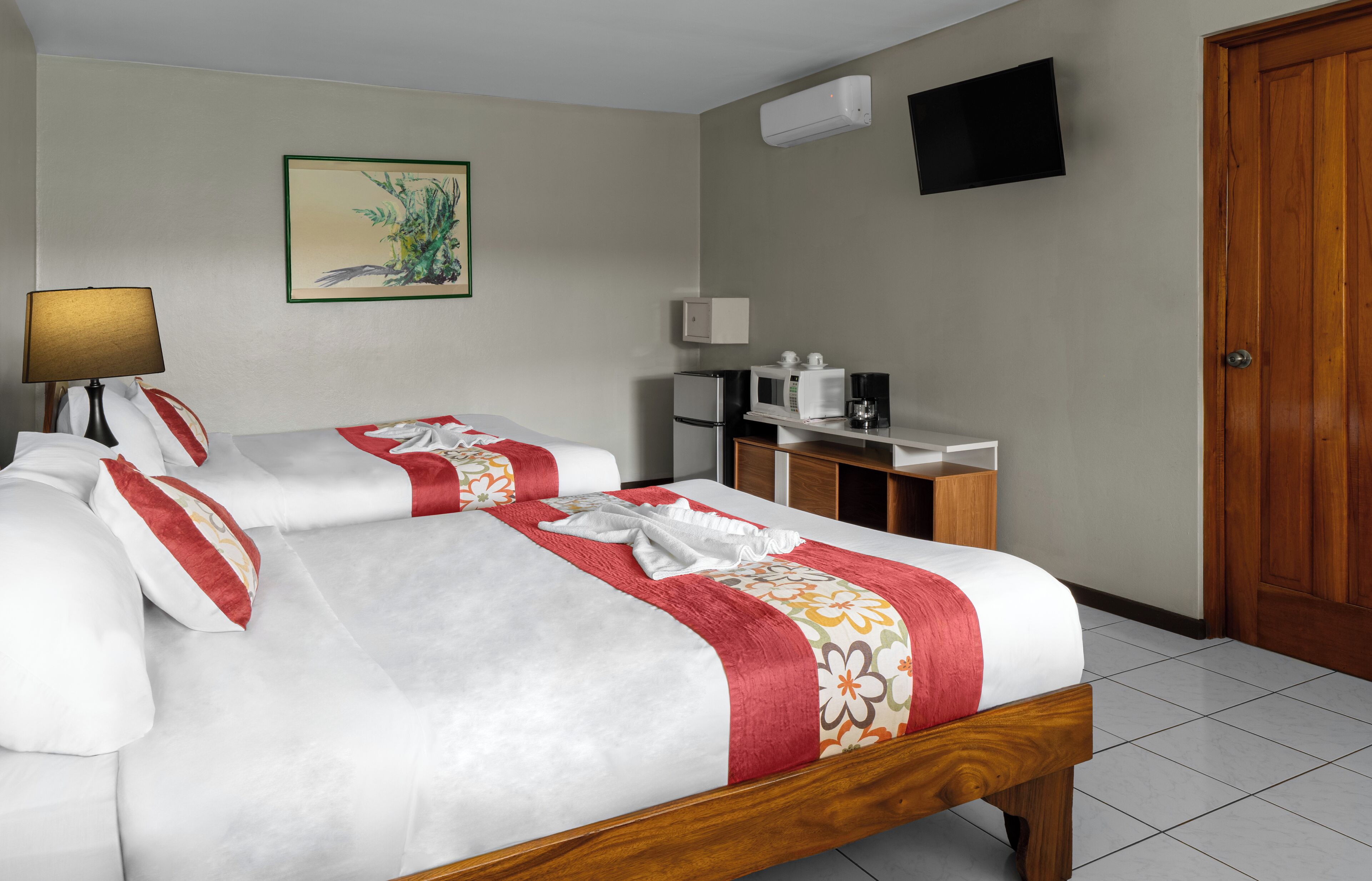 A hotel room with a bed, a desk, a microwave, a refrigerator, a TV, and a door.