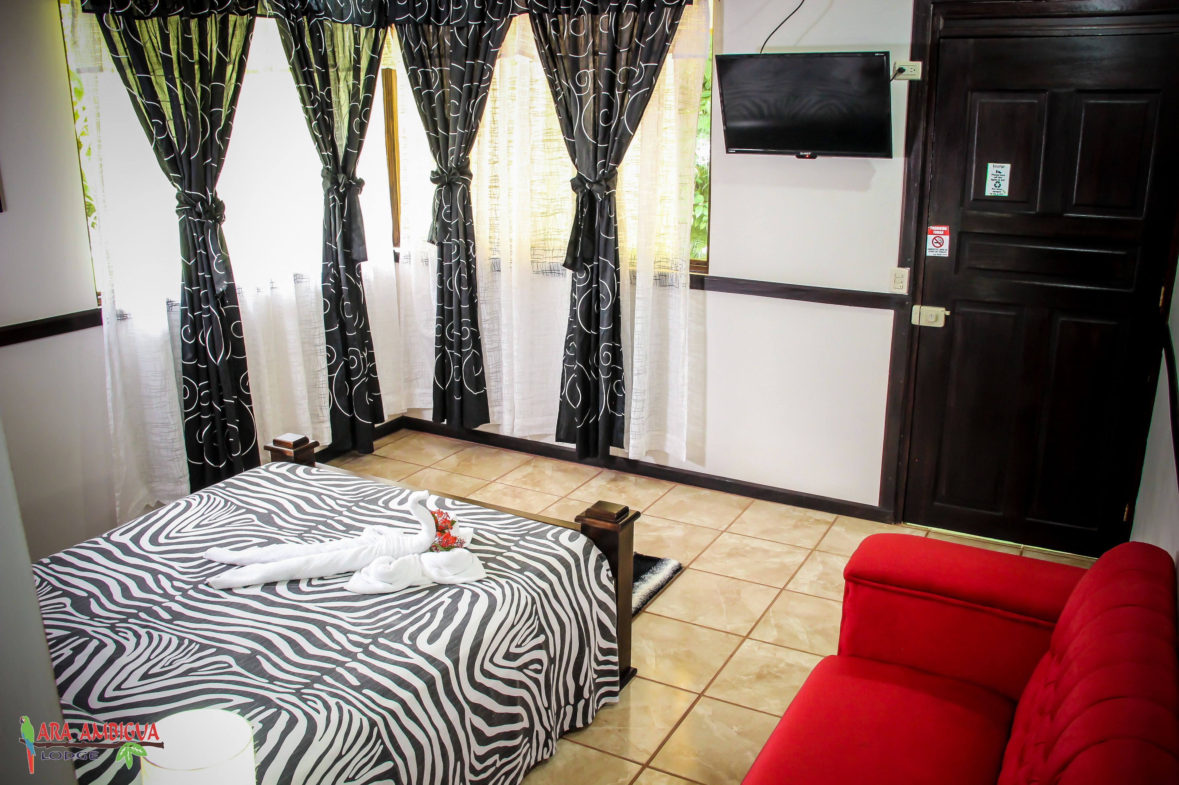 A hotel room with a zebra-patterned bed, a red sofa, and curtains with a black and white design.