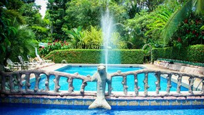 Une piscine ornée d’une statue de sirène, entourée d’une végétation luxuriante et d’un garde-corps en pierre décoratif.