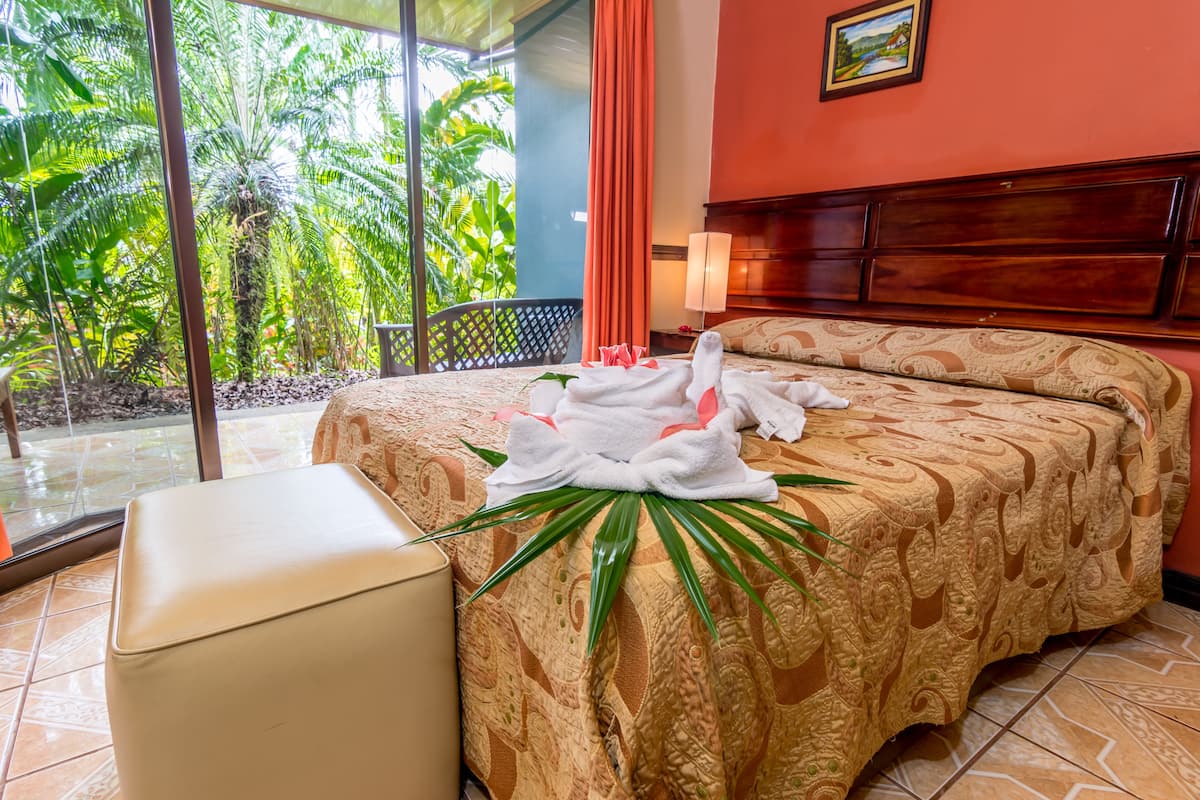 Une chambre d’hôtel avec un lit, une fenêtre donnant sur un espace verdoyant, une table de chevet et une petite table de nuit.