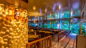 Un restaurant aux murs de pierre, aux tables et aux chaises en bois. Il possède de grandes fenêtres donnant sur un paysage verdoyant.