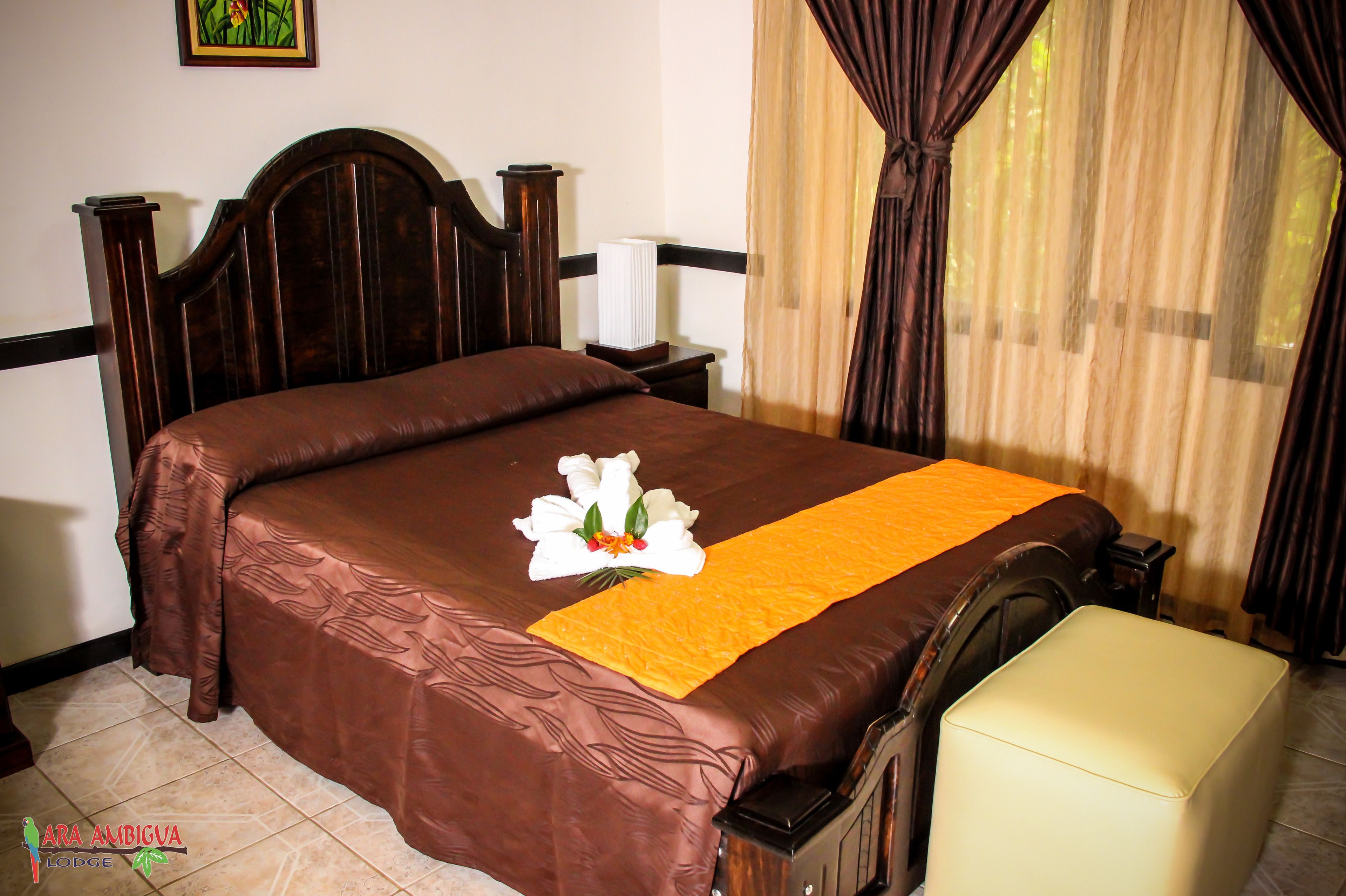 A neatly made bed with a brown bedspread, a white flower arrangement, and a yellow runner.