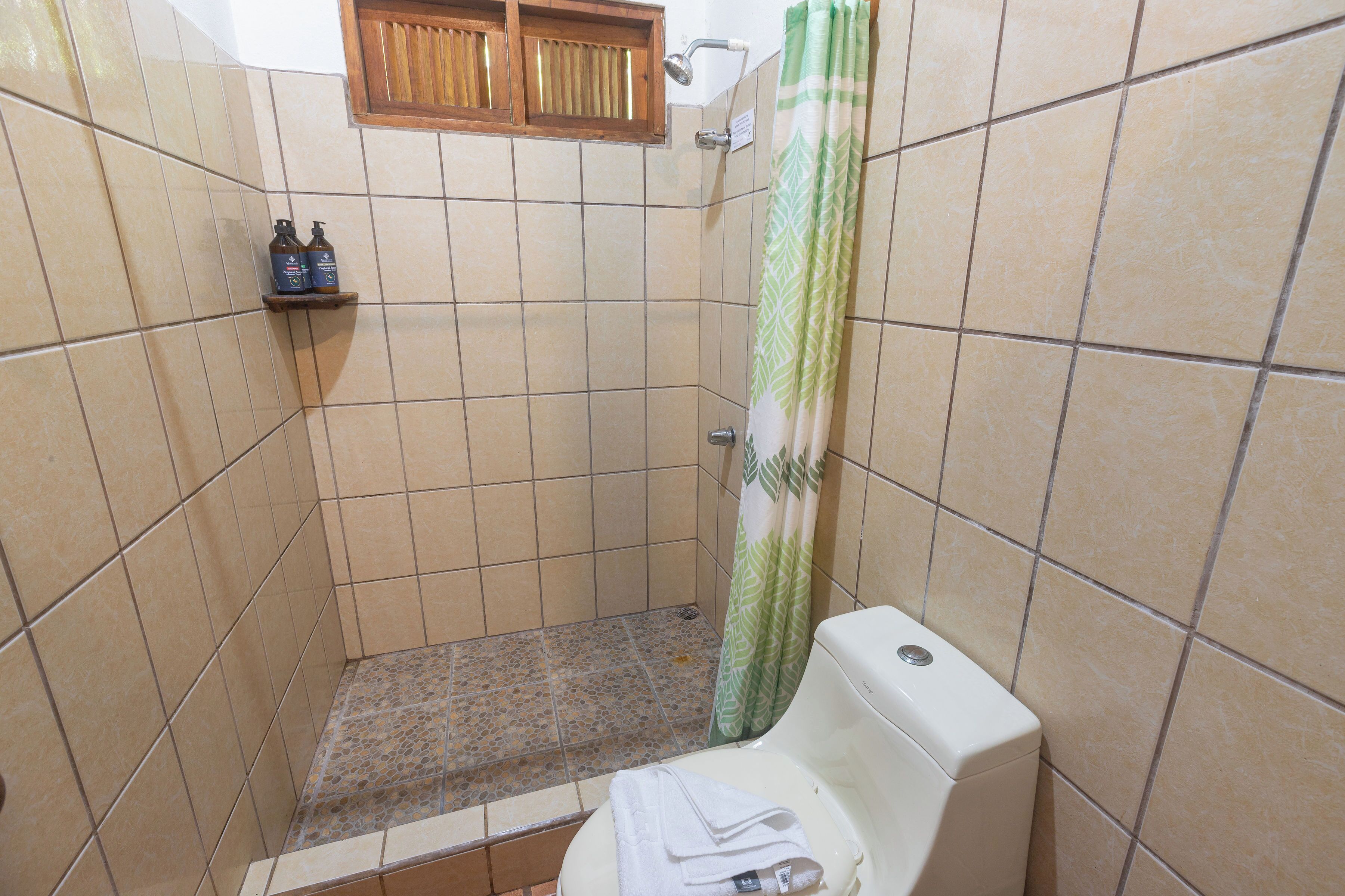 A bathroom with a shower, toilet, and shelf with toiletries.