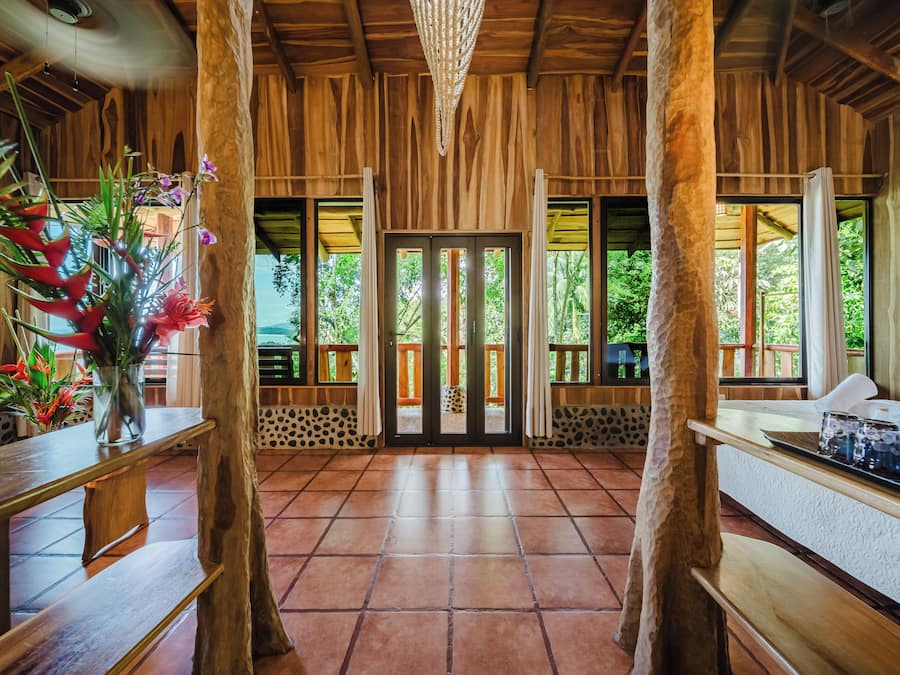 A wooden interior with a tiled floor, a central door, and a view of greenery outside.
