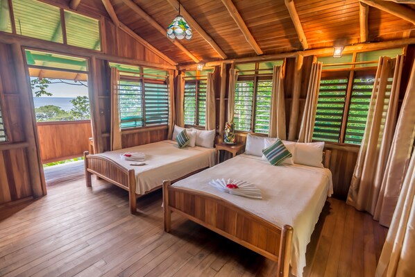 A wooden cabin with two beds, a wooden floor, and large windows with curtains. - La Cusinga Lodge (Bahía Ballena)