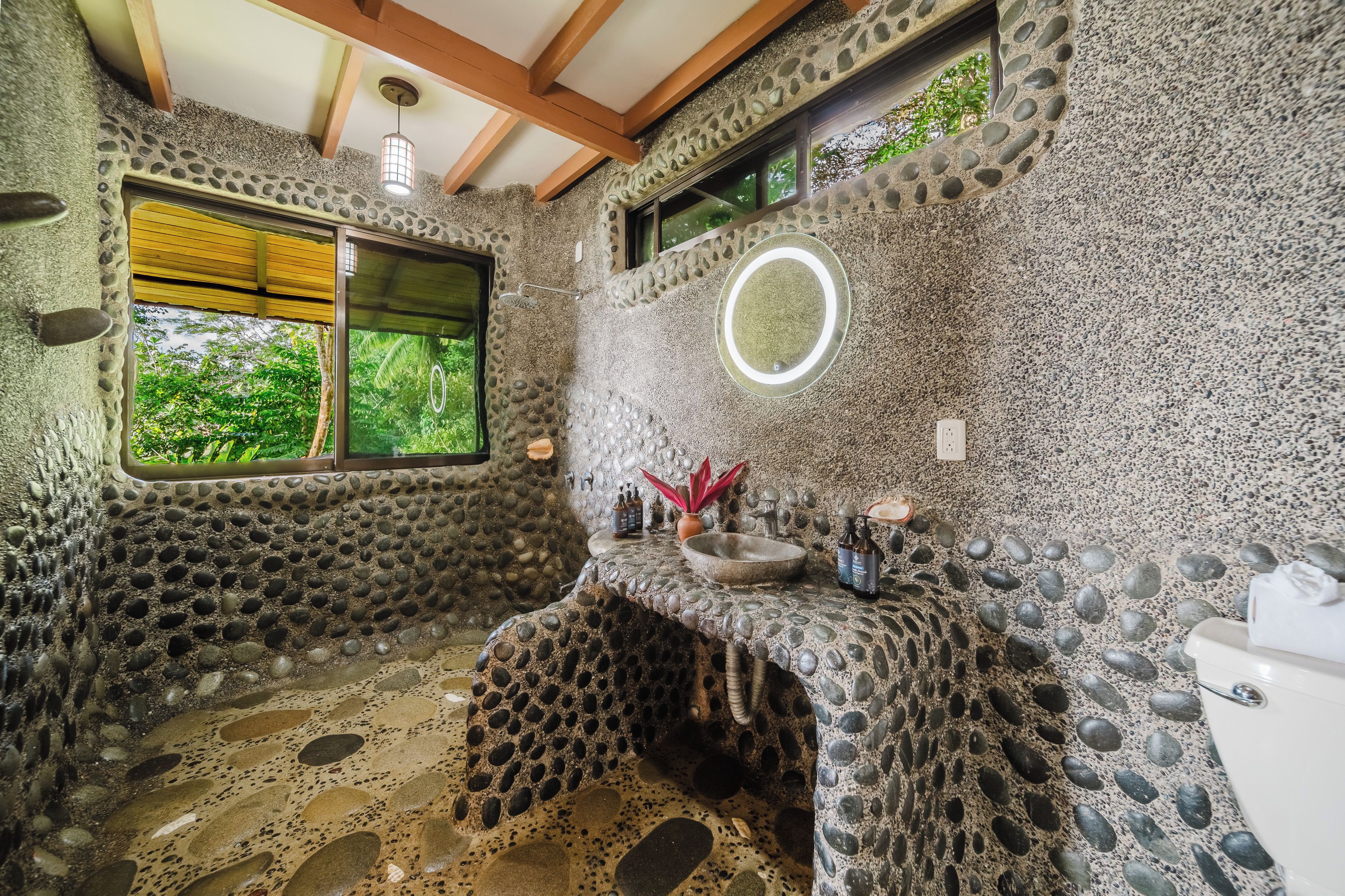 Ein Badezimmer mit Steinwand, Fenster, Waschbecken und Dusche.