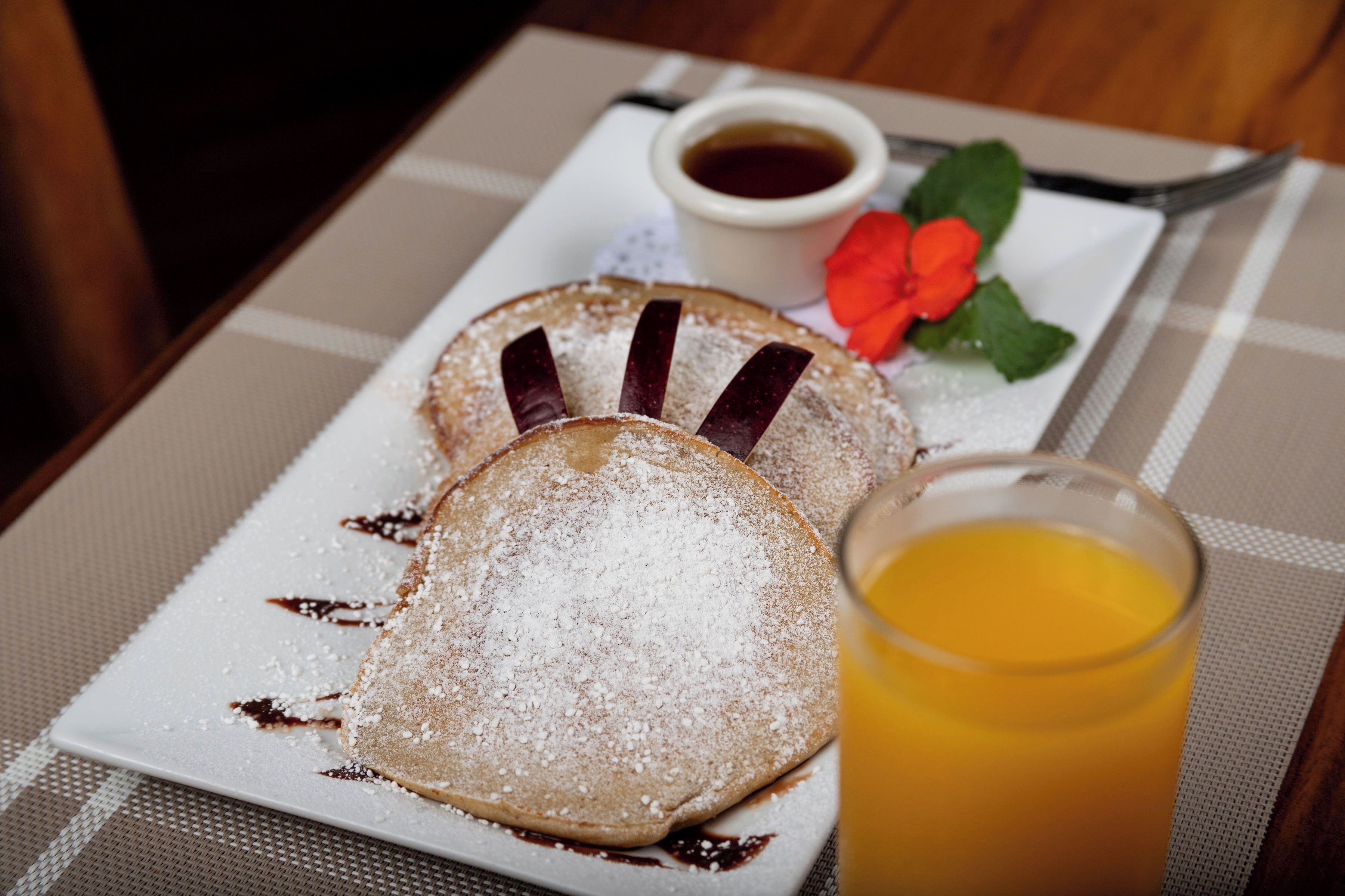 A breakfast plate with pancakes, syrup, powdered sugar, and a small cup of coffee.