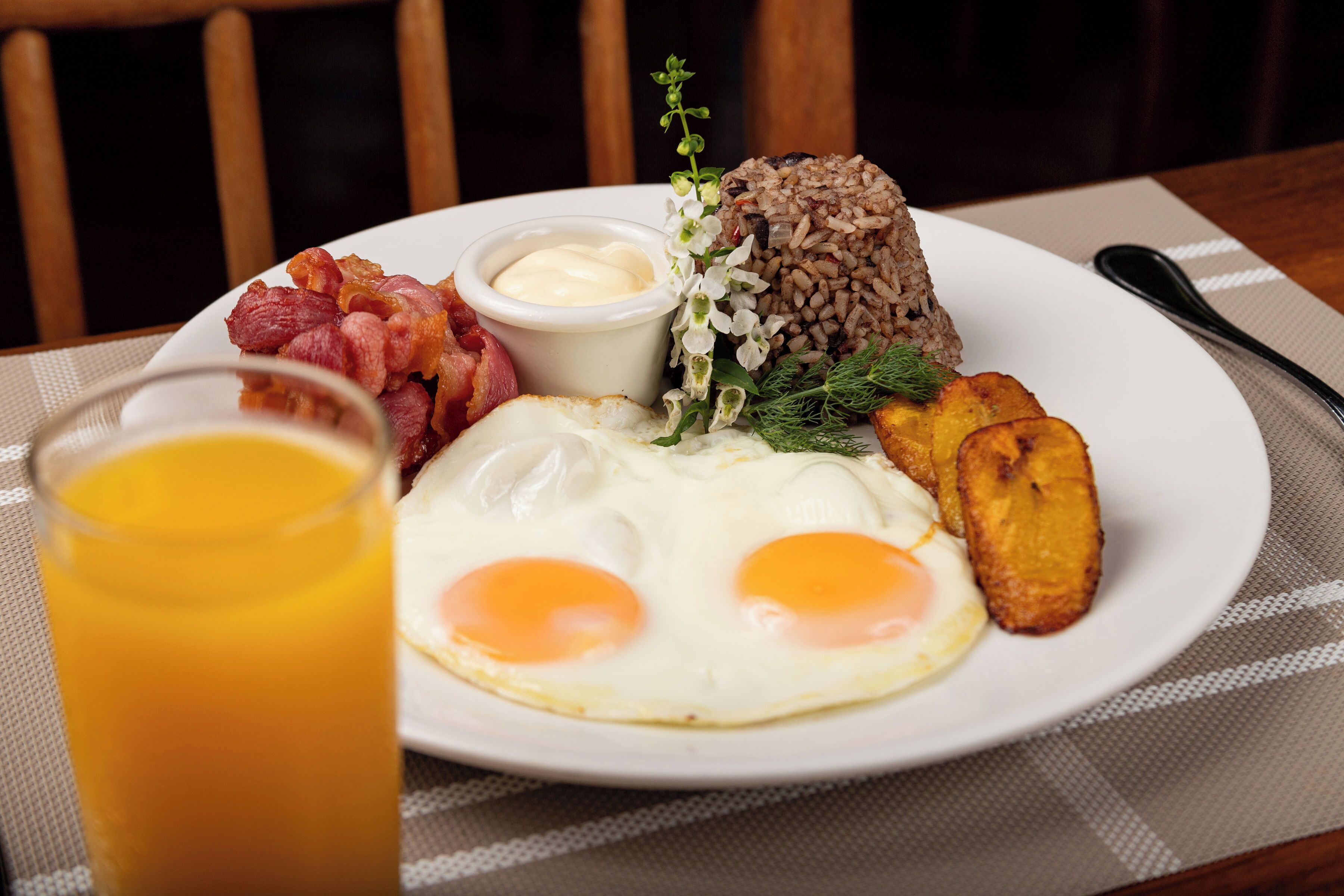 En tallerken med æg, bacon, ristet brød og et glas appelsinjuice.
