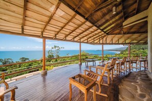A wooden deck with tables and chairs overlooking a scenic ocean view. - La Cusinga Lodge (Bahía Ballena)