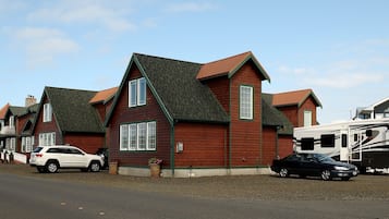 A row of red wooden houses with green trim and green roofs, a white RV, and a black car parked in front.