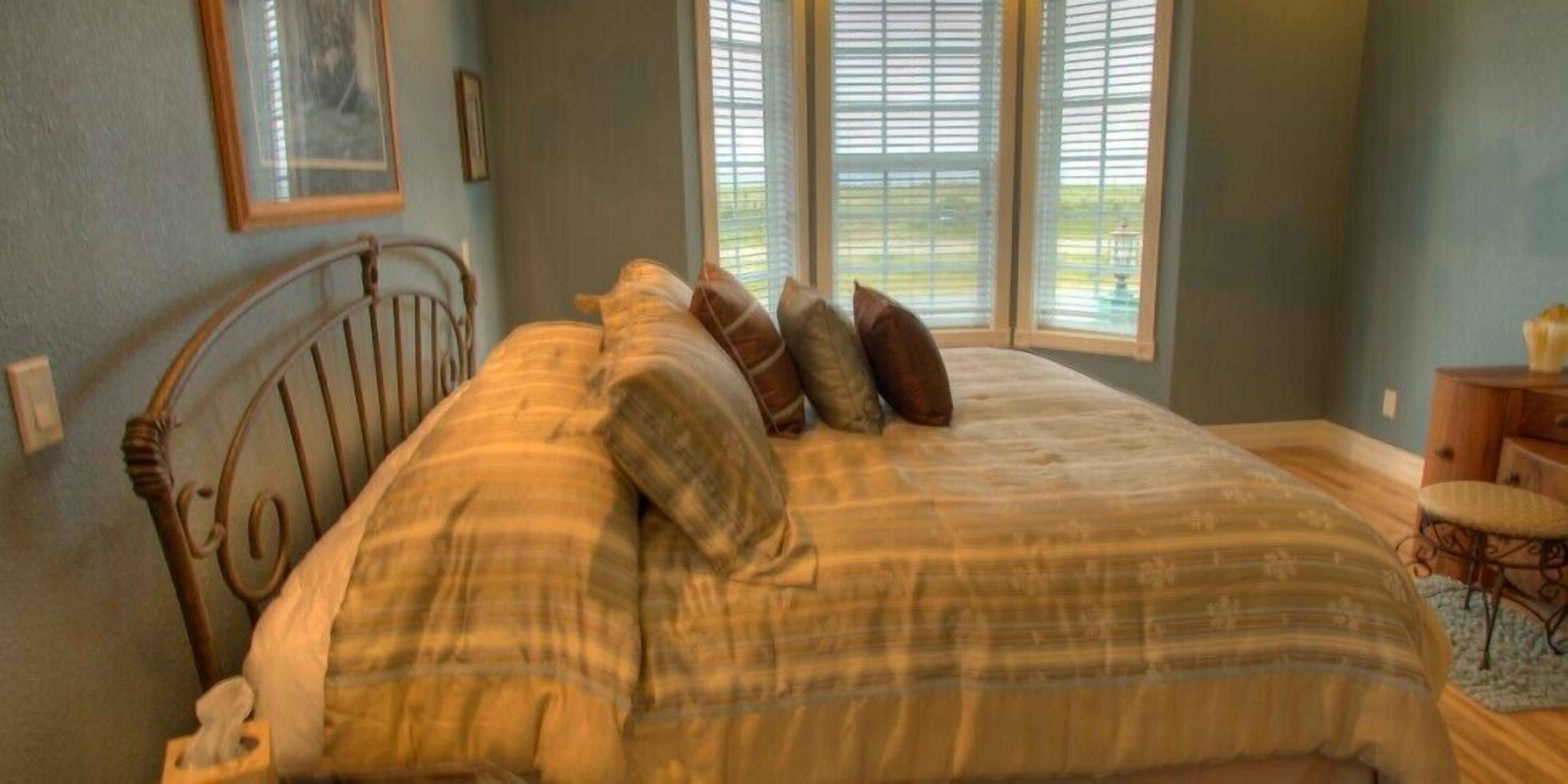 A bedroom with a bed, pillows, a nightstand, and a window with blinds.