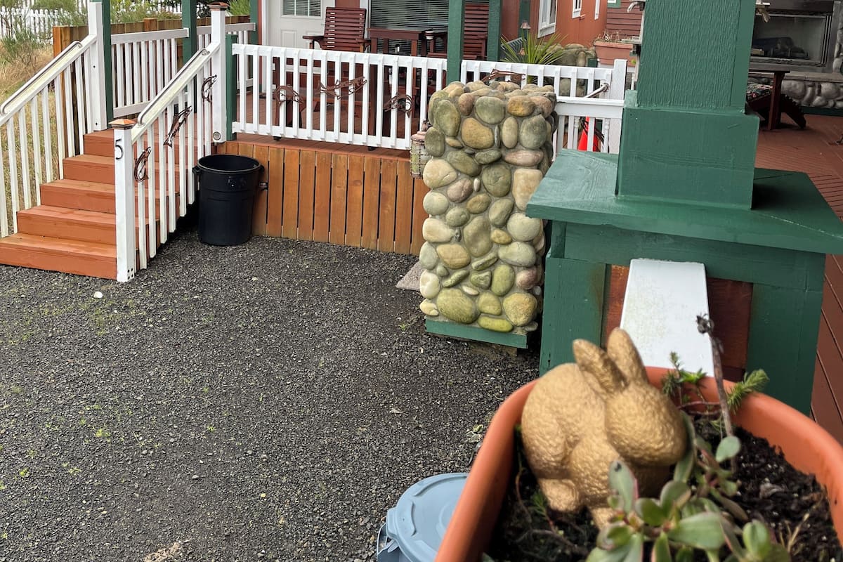 A wooden building with a porch, a stone wall, and a small garden area with a rabbit statue.