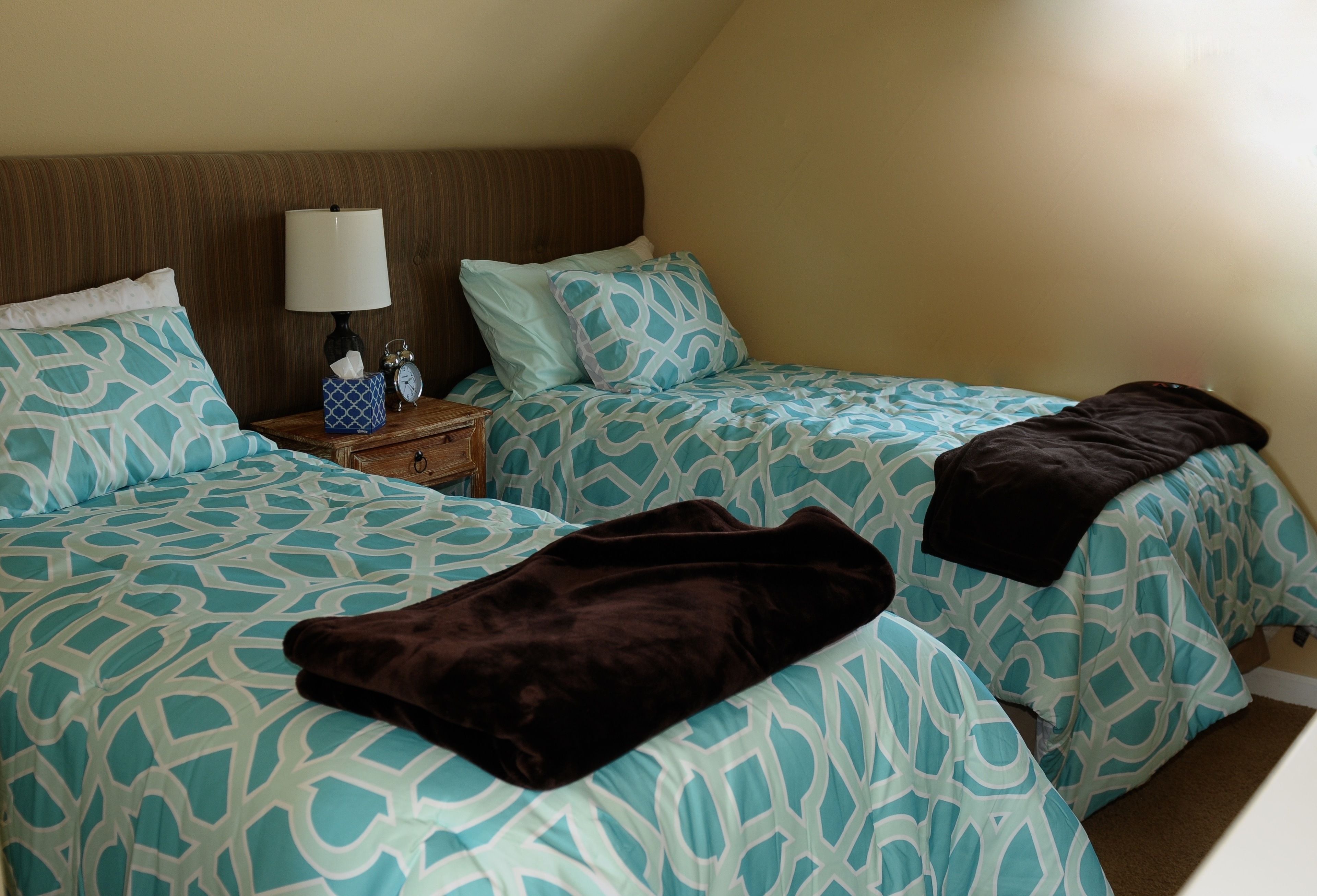 A bedroom with two beds, each with patterned bedding, a bedside table with a lamp, and a clock.