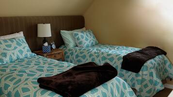 A bedroom with two beds, each with patterned bedding, a bedside table with a lamp, and a clock.