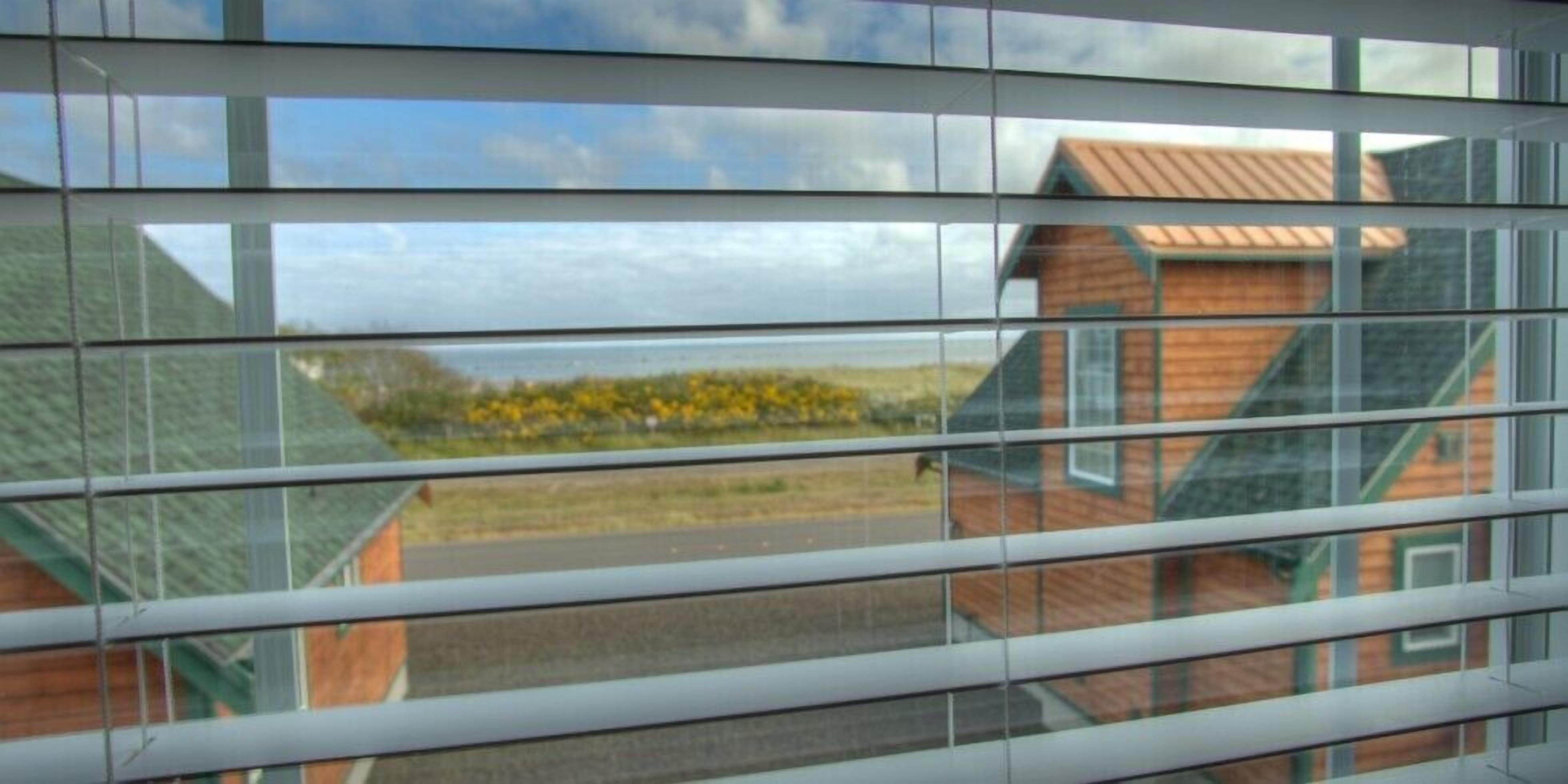 A view through a window with horizontal blinds, revealing a building with a sloped roof and a wooden exterior.