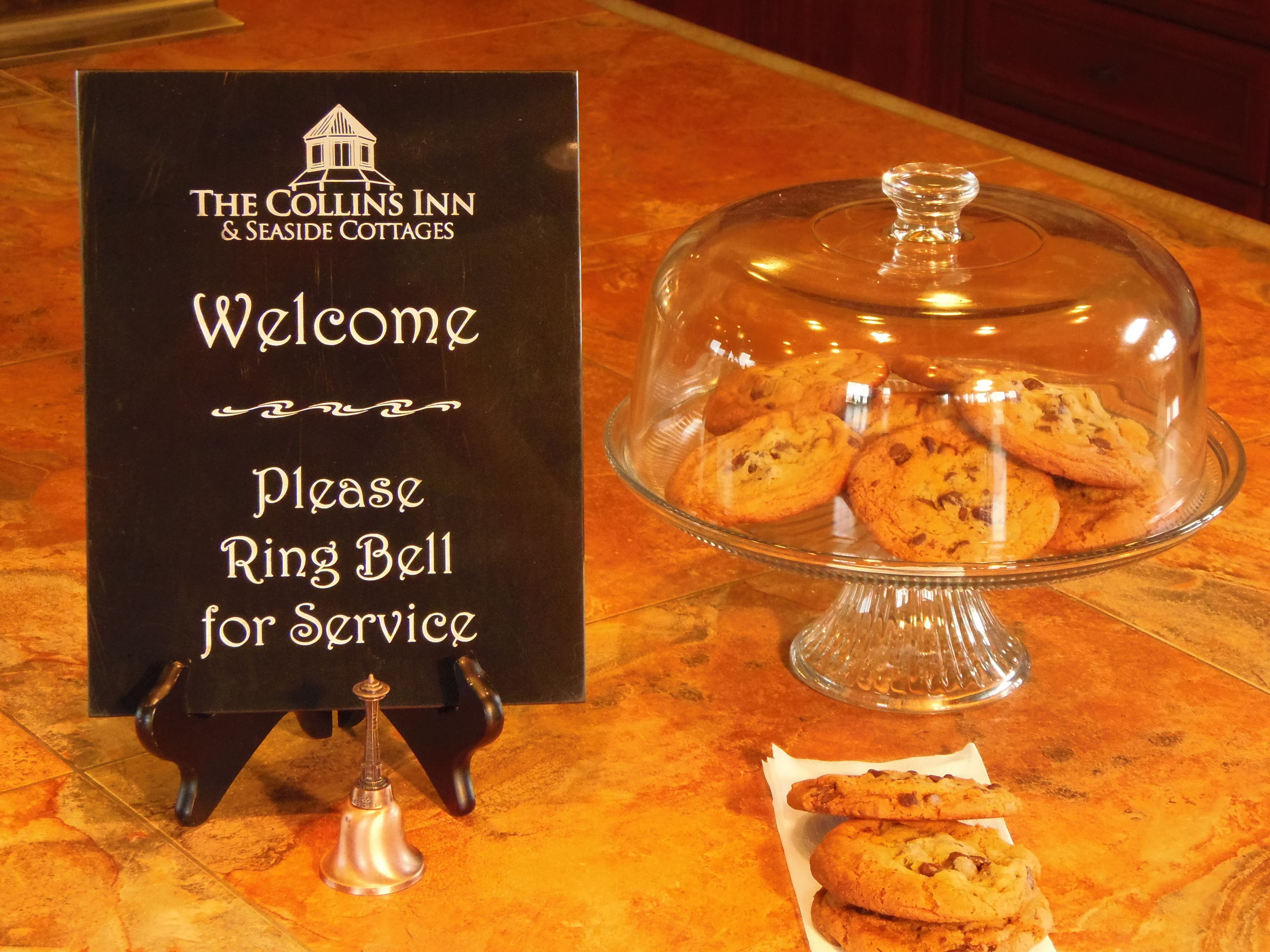 A signboard with the text "The Collins Inn & Seaside Cottages Welcome Please Ring Bell for Service" and a glass display case with cookies.