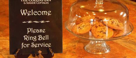 Een bord met de tekst 'The Collins Inn & Seaside Cottages Welkom, bel voor service' en een glazen vitrine met koekjes.