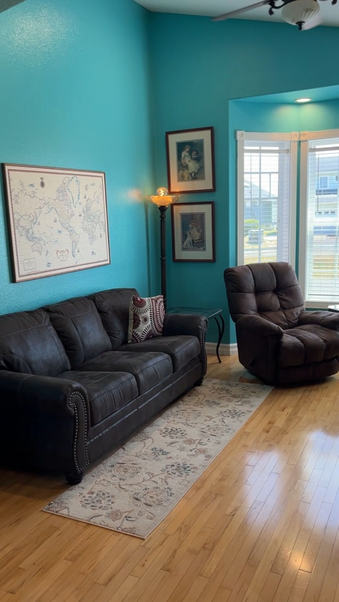 A living room with a teal wall, a black leather sofa, a patterned rug, and a wooden floor.