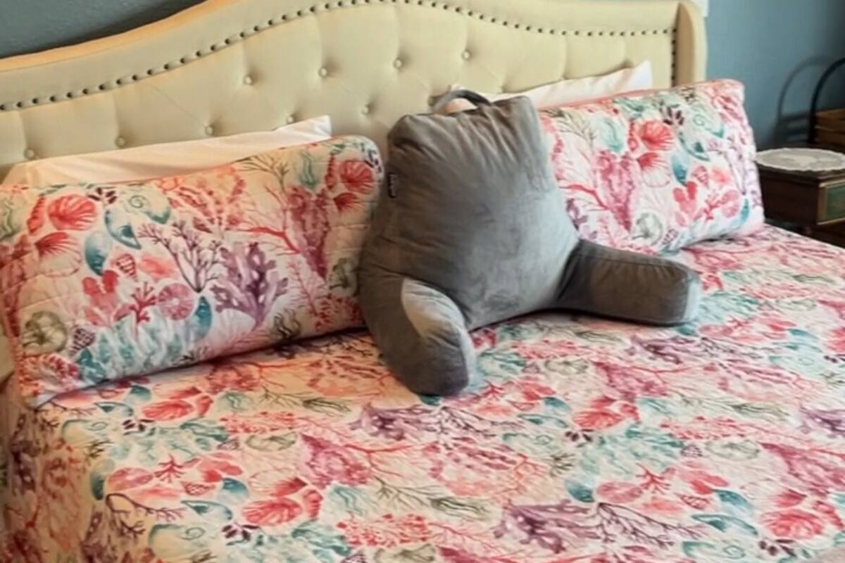 A bed with a floral bedspread, a grey pillow, and a framed picture of a ship on the wall.