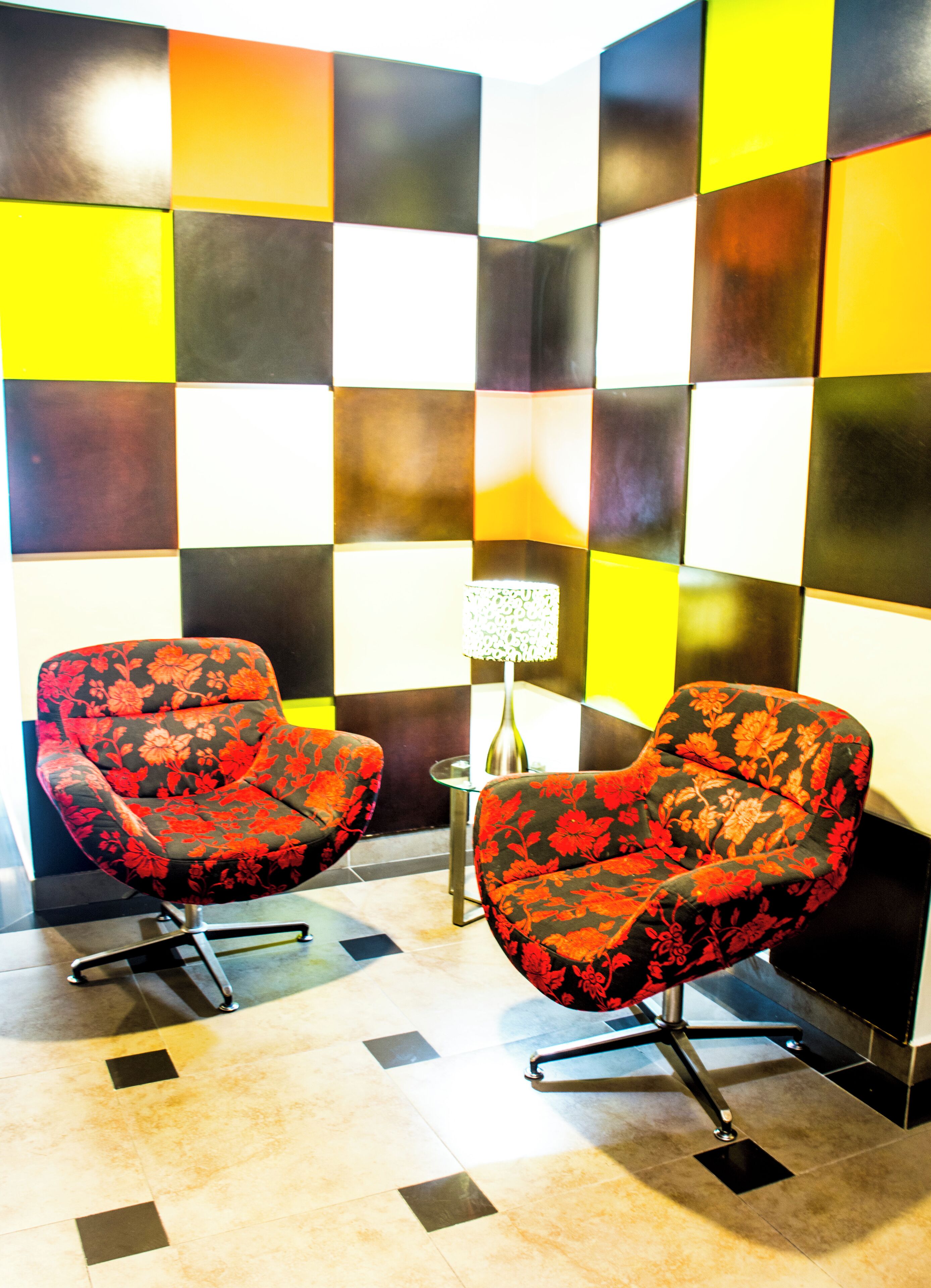 Une pièce comprenant deux fauteuils à motifs floraux, une petite table avec une lampe et un motif à carreaux sur le mur.
