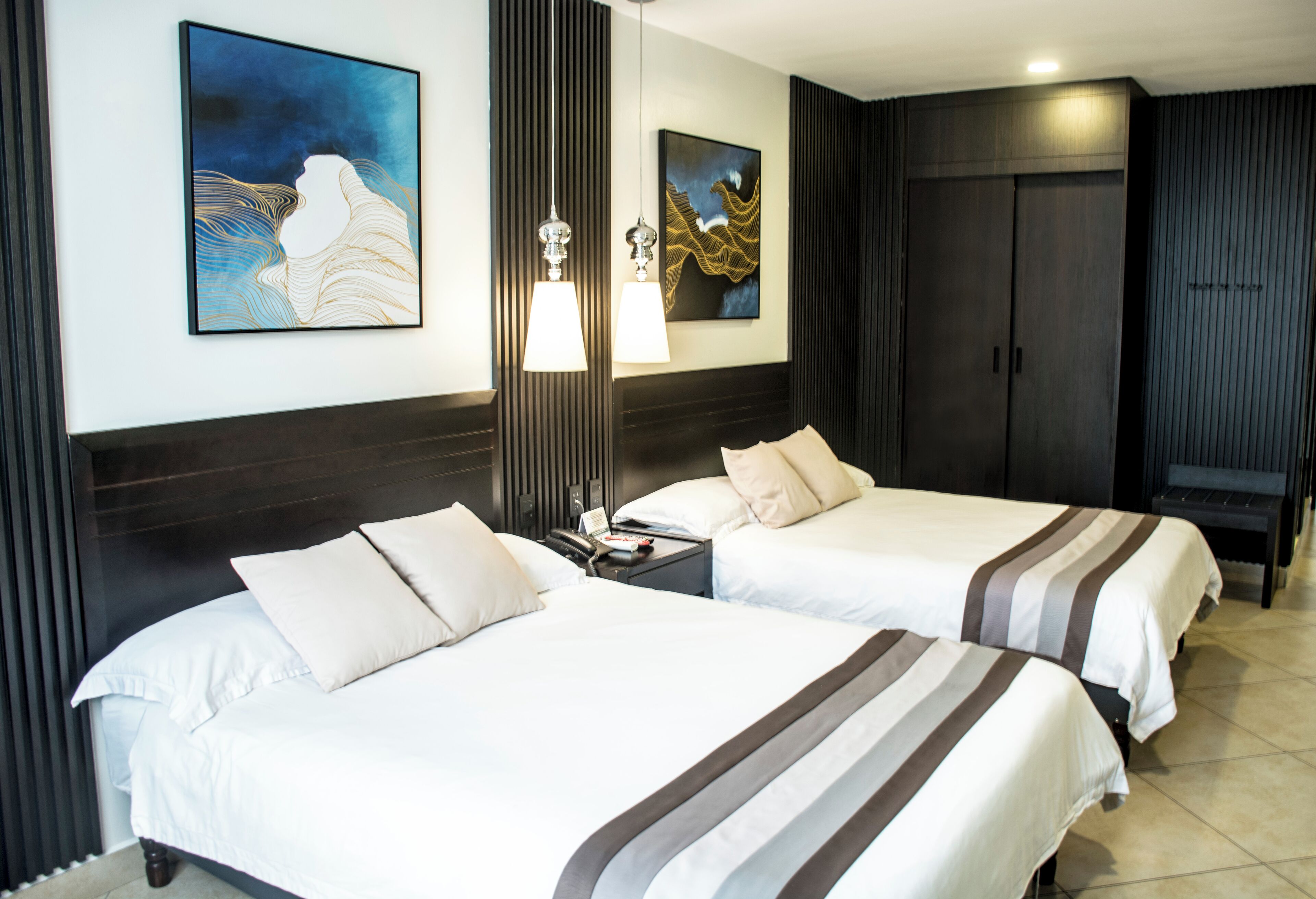 Habitación de hotel con dos camas, una mesita de noche, una lámpara y obras de arte en las paredes.