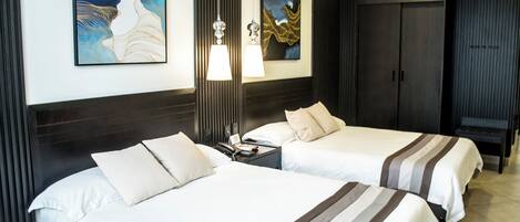 Habitación de hotel con dos camas, una mesita de noche, una lámpara y obras de arte en las paredes.